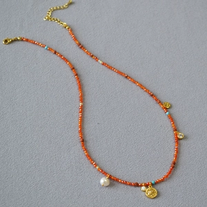 Detail of orange faceted beads necklace with gold coin pendant and freshwater pearl