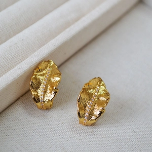 Gold leaf stud earrings with brushed texture and sparkling zircon inlay on fabric