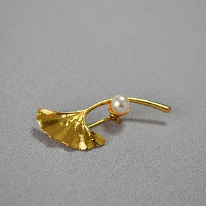 Detailed close-up of golden ginkgo leaf brooch with a glossy pearl on fabric