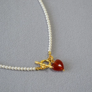 Detailed macro view of white pearl necklace with golden OT buckle and red heart pendant