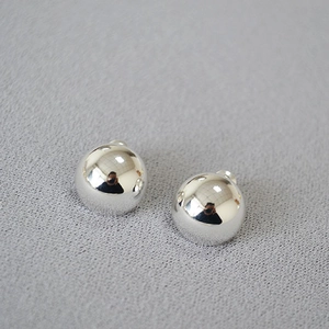 Minimalist silver spherical stud earrings with polished mirror finish on gray texture