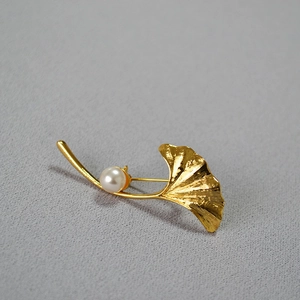 Detailed macro shot of a brushed gold ginkgo leaf brooch with a white pearl accent