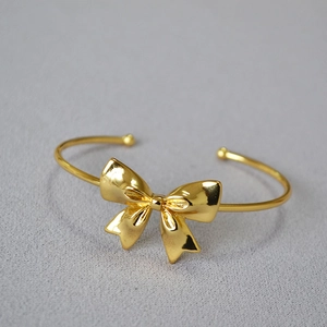 Close-up of polished gold-plated bow cuff bracelet with adjustable open design