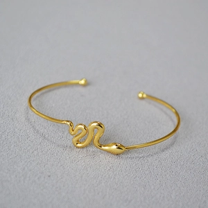 Detail of a thin gold snake-shaped bangle with rounded ends on a textured gray background