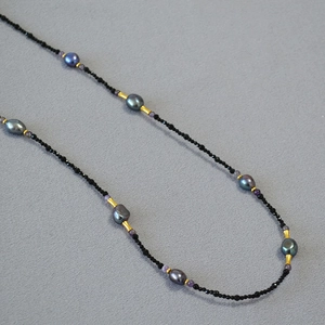 Macro shot of long beaded necklace with black spinel and baroque pearls on grey surface
