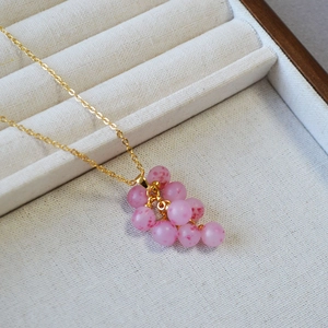 Vue rapprochée du pendentif grappe de perles roses avec chaîne dorée sur plateau