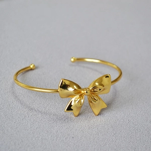 Minimalist gold-plated bow cuff bracelet with rounded ends on light textured fabric