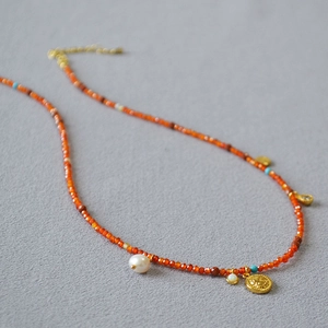 Detailed view of red agate beads with a baroque pearl and gold coin pendant necklace