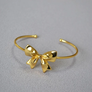 Detailed macro view of gold plated bow bracelet with adjustable open cuff design