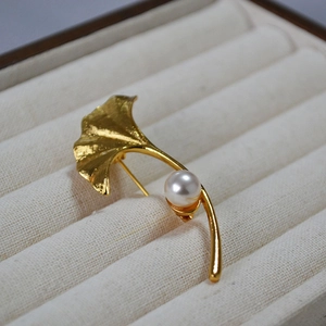 Close-up of golden ginkgo leaf brooch with brushed texture and a round white pearl