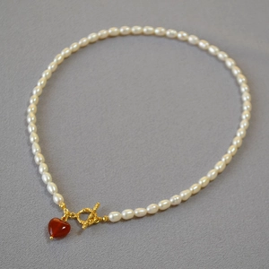 Detailed close-up of pearl necklace featuring red heart pendant and golden OT clasp design