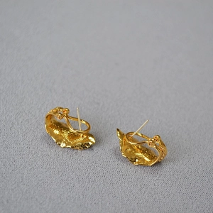 Detail of gold-plated leaf earrings with vintage texture and sparkling zircons