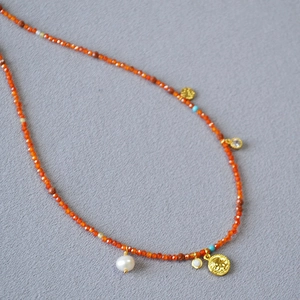 Detail of red beaded necklace with irregular pearl and gold coin pendant design