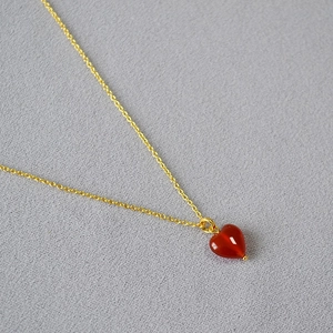 Detailed macro view of heart-shaped red agate pendant on a thin gold-tone chain necklace