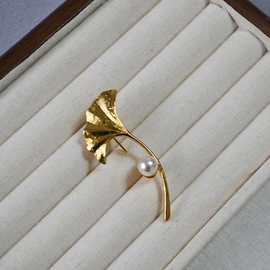 Close-up of golden ginkgo leaf brooch with a white pearl on a velvet jewelry display tray