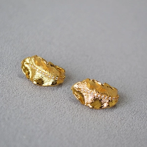 Macro detail of leaf-shaped gold stud earrings with cubic zirconia and brushed metal texture