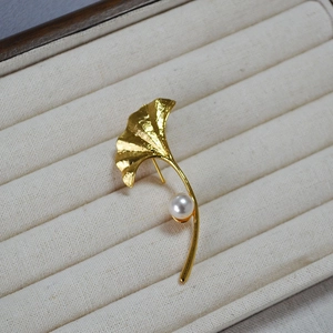 Detailed view of golden ginkgo leaf brooch with brushed texture and a white pearl accent