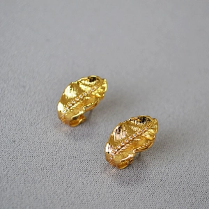 Macro shot of gold leaf earrings with textured veins and sparkling zircon stones