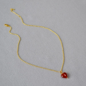 Close-up of a polished red agate heart pendant on a delicate golden link chain