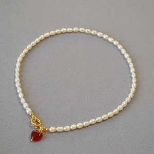 Elegant pearl necklace with gold OT buckle and red heart agate pendant on gray surface