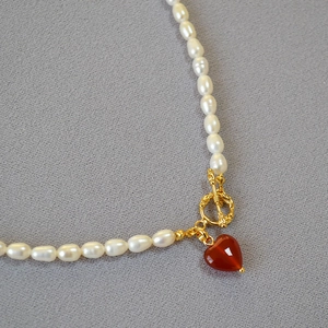 Detailed close-up of pearl necklace with red heart agate pendant and golden OT clasp