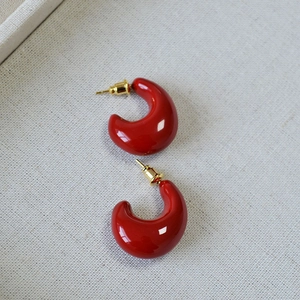 Detailed view of red drop-shaped enamel earrings with glossy finish and gold posts
