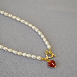 Macro shot of freshwater pearl necklace featuring a gold OT clasp and red heart pendant