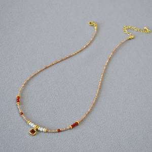 Detail of beaded necklace with freshwater pearls, red gemstones and gold clasp closure