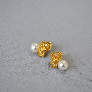 Detail of golden rose earrings with crystals and white pearls on grey textured fabric
