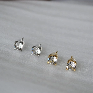 Macro view of silver and gold round stud earrings with four-prong crystal settings