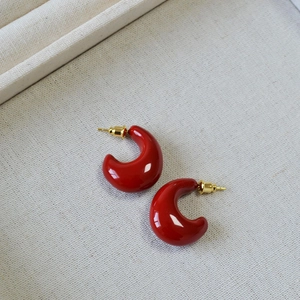 Glossy red C-shaped enamel earrings with gold butterfly backings on a linen tray