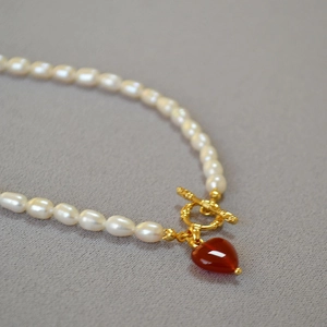 Close-up of pearl necklace with gold OT clasp and red heart agate pendant detail