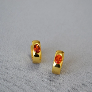 Detail view of gold-plated brass hoop earrings with oval orange-red gemstones