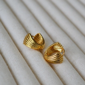Detailed close-up of gold-plated shell-shaped hoop earrings with textured vertical ridges