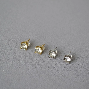 Macro detail of silver and gold stud earrings with round-cut crystals in four-prong settings