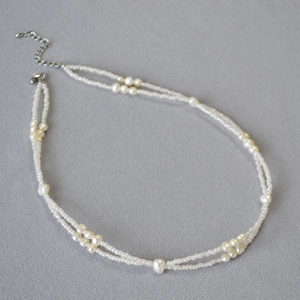 Detail of double-layer necklace with Baroque pearls and tiny white beads on grey surface