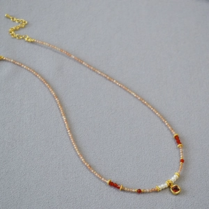 Detail of beaded necklace with freshwater pearls, red agate, and a faceted gemstone pendant
