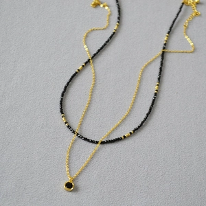 Détail d'un collier doré double rang avec pendentif carré noir et perles de spinelle