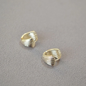 Macro detail of silver shell-shaped earrings with radial texture on gray fabric