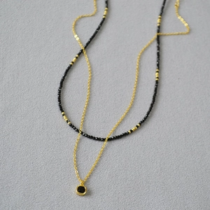 Détail du collier double couche avec pendentif carré noir et chaîne à perles dorées