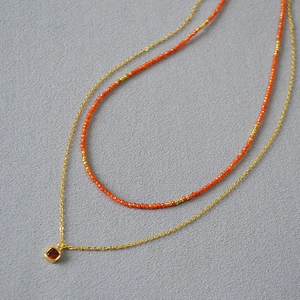 Detail of double-layer necklace featuring orange-red beads and a square red gemstone pendant