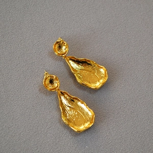 Detail of gold leaf-shaped earrings with irregular hammered texture and organic design