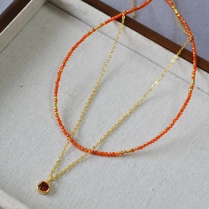 Detail showing double-layered gold necklace with orange beads and red square gemstone pendant