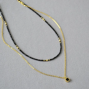 Gros plan sur le collier double rang avec perles spinelle noires et pendentif carré doré