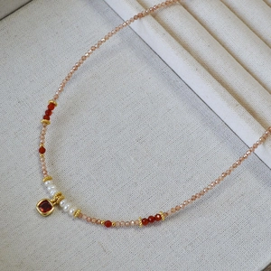 Close-up of beaded necklace with champagne zircons, pearls and a red square gemstone pendant