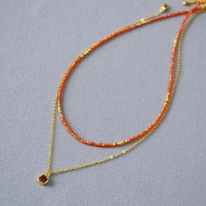 Detail of double-layer necklace with orange beads and red square gemstone pendant