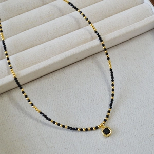 Détail macro d'un collier en perles de spinelle noire avec un pendentif carré doré