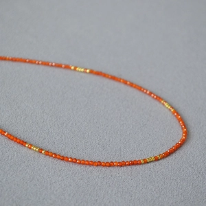 Macro shot of 2mm orange-red beaded necklace with small gold accents on gray fabric