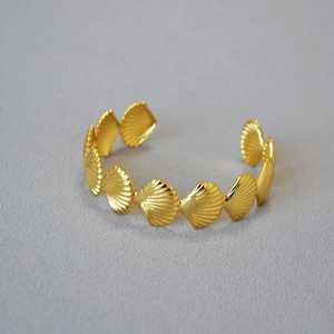 Macro detail of golden brass open cuff bracelet featuring linked seashell patterns