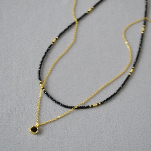Détail d'un collier double rang avec perles noires et pendentif carré sur tissu gris